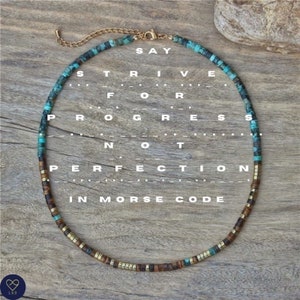May include: A turquoise and brown beaded necklace with gold accents. The beads spell out the phrase "SAY STRIVE FOR PROGRESS NOT PERFECTION IN MORSE CODE".