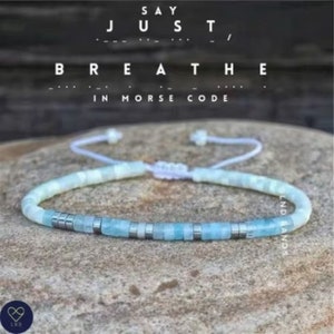 May include: A light blue beaded bracelet with silver beads and a white cord. The bracelet says "Say Just Breathe" in Morse code.