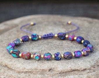 May include: A purple and blue gemstone bracelet with gold accents and a purple cord. The bracelet is made with small, oval-shaped beads and has a sliding knot closure. @LND_BANDS
