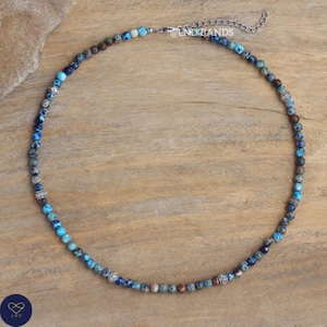 May include: A necklace made of blue, turquoise, and brown beads, with silver-coloured metal accents and a chain clasp. The text "@LND-BANDS" is visible on the chain.