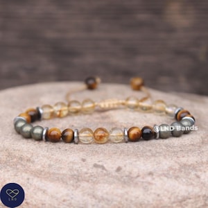 Könnte beinhalten: Ein Armband mit braunen, goldenen und silbernen Perlen. Das Armband hat einen verschiebbaren Knotenverschluss.