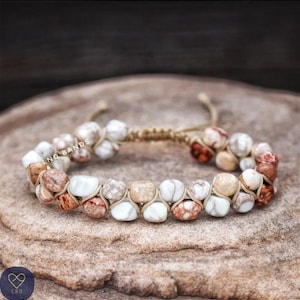 Puede incluir: Un brazalete de piedra blanca y marrón con cierre de cordón anudado. El brazalete presenta una variedad de piedras con patrones marrones y blancos.