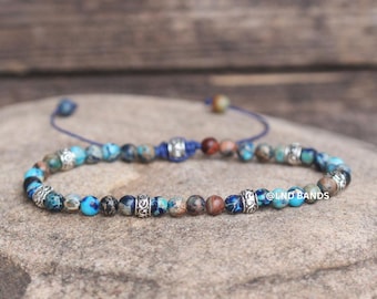 May include: A beaded bracelet featuring round, multi-colored stones in shades of blue, brown, and grey, interspersed with ornate silver-toned metal spacers. The bracelet includes a blue cord closure and displays the text @LND BANDS on the side.