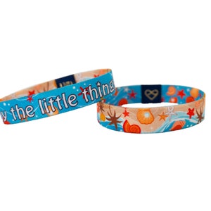 May include: Two blue and white woven wristbands with a seashell and starfish pattern. One wristband has the text "Enjoy the little things" printed on it.