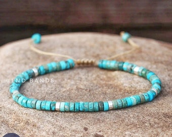 May include: Turquoise beaded bracelet with silver accents and a brown cord closure. The bracelet is on a brown stone surface. @LND BANDS
