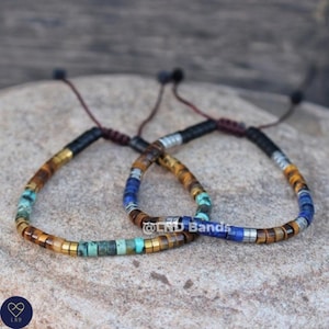 May include: Two beaded bracelets featuring a combination of brown, gold, blue and turquoise beads. The bracelets have a sliding knot fastening.