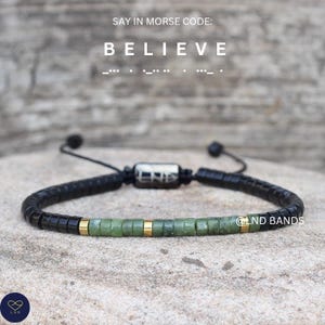 May include: Black beaded bracelet with green and gold details. The bracelet features the word "BELIEVE" in Morse code. It has an adjustable design and a metal clasp. The brand name "LND Bands" is visible.