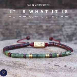 Op de afbeelding: Een kralenarmband met een mix van groene, bordeauxrode en goudkleurige kralen. De armband heeft een goudkleurige rechthoekige sluiting met de letters "LND". De tekst "IT IS WHAT IT IS" staat in morsecode boven de armband.