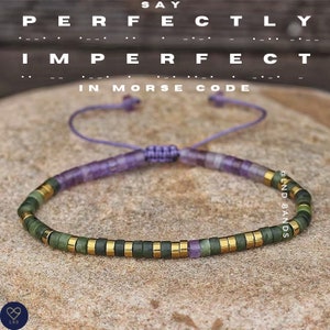 Könnte beinhalten: Ein violettes und grünes Perlenarmband mit goldenen Akzenten. Das Armband besteht aus kleinen, runden Perlen und hat einen einfachen, verstellbaren Verschluss. Das Armband ist in Morsecode als "Say Perfectly Imperfect" geschrieben.