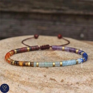 May include: A colorful beaded bracelet with a chakra design. The bracelet features a spectrum of colors, including red, orange, yellow, green, blue, and purple, with gold-colored spacers. The bracelet is on a neutral background.