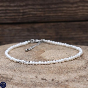 May include: A delicate bracelet composed of small, white, irregularly shaped freshwater pearls strung together. The piece features a silver-toned metal chain extension with a lobster claw clasp. The text LND BANDS is printed on the image.