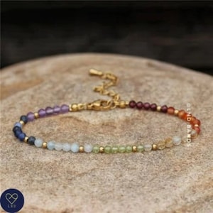 May include: A gold chain bracelet with a clasp closure. The bracelet is made of small, round beads in a rainbow of colors, including purple, blue, green, yellow, orange, and red.