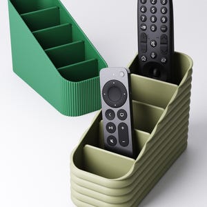 May include: Two plastic desk organizers with ribbed exterior textures and four internal compartments each. One organizer is dark green, and the other is light olive green, holding a black television remote and a grey streaming device remote.