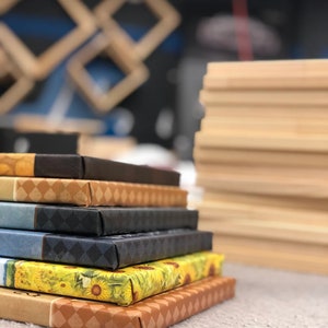 May include: A stack of six canvas prints with various designs, including a sunflower pattern, a brown and white geometric pattern, and a blue and black geometric pattern. The prints are stacked on a light gray surface.