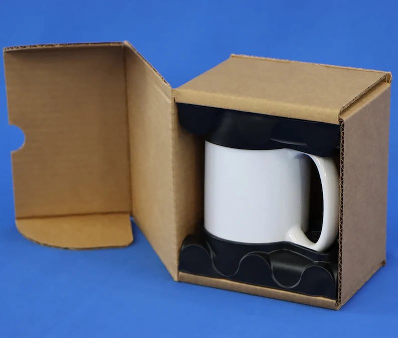 Puede incluir: Una taza de cer&aacute;mica blanca con asa negra est&aacute; empaquetada en una caja de cart&oacute;n marr&oacute;n con un inserto de espuma negra.