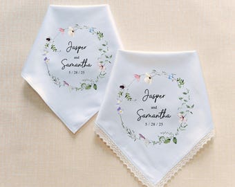 May include: Two white handkerchiefs with floral wreath designs. Each handkerchief features a wreath of flowers and greenery, with the names "Jasper and Samantha" and the date "5/28/25" printed in black. One handkerchief has a lace trim.