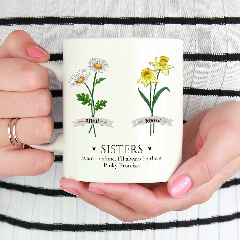 Puede incluir: Taza de cer&aacute;mica blanca con un dise&ntilde;o floral con margaritas y narcisos. La taza tiene los nombres "anna" y "rebecca" escritos en ella, junto con el texto "&bull; SISTERS &bull; Rain or shine, I'll always be there Pinky Promise."