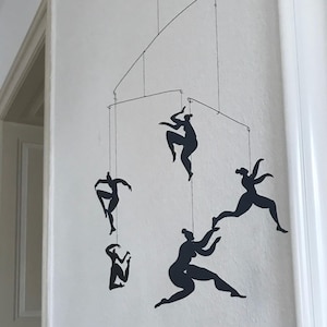 Puede incluir: Un móvil con cinco figuras de personas en silueta negra en varias poses, colgando de un techo blanco.