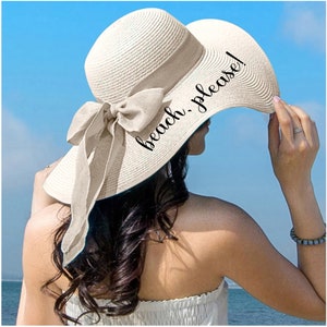 May include: A white sun hat with a wide brim and a bow. The hat has the text "beach, please!" embroidered on the brim.