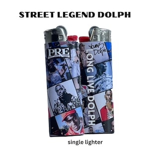 May include: A black and silver lighter with a collage of images of rapper Young Dolph. The lighter has the words "PRE" and "LONG LIVE DOLPH" printed on it.