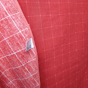 Puede incluir: Tela roja con un patrón de cuadrícula de líneas y puntos blancos. La tela está doblada, revelando un patrón blanco y rojo contrastante en el interior. Una etiqueta con la palabra "IKEA" es visible.