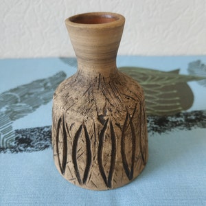 Può includere: Un piccolo vaso in ceramica marrone con un design testurizzato e scolpito. Il vaso ha una base larga e un collo stretto.