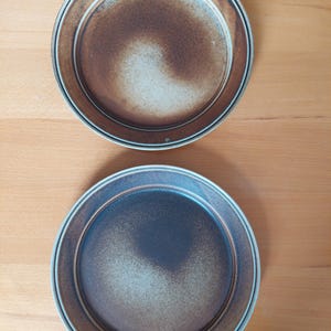 May include: Two ceramic plates with a brown and white speckled glaze. The plates have a raised rim and a slightly scalloped edge.