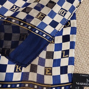 Op de afbeelding: Een blauwe en witte geruite zijden sjaal met gouden letters die "Marko" en "100% zijde Droog reinigen alleen" zeggen.