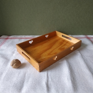 May include: A wooden tray with heart-shaped cutouts and handles. The tray is light brown and has a natural wood finish.