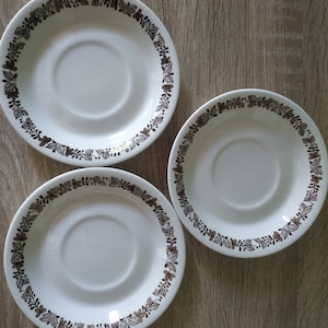 Puede incluir: Tres platillos de cerámica blanca con un diseño floral marrón alrededor del borde.