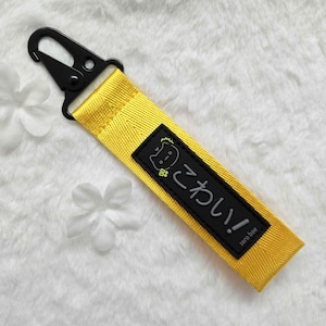 Può includere: Un portachiavi giallo con una toppa nera che dice "ねこちゃん!" e "zero bae" in giapponese e inglese.