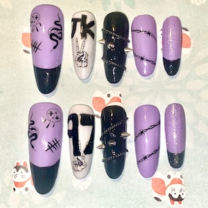 May include: Set of ten purple and black press-on nails with various designs. The designs include a snake, a peace sign, barbed wire, a skull, and the letters "TK".