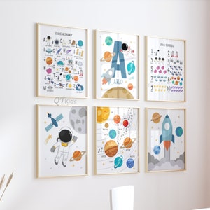 May include: A set of six space-themed educational posters for children. The posters feature an alphabet, numbers, planets, astronauts, and rockets. The posters are printed on white paper with colourful illustrations and are framed in gold.