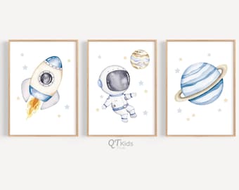 May include: Set of three watercolor prints featuring an astronaut floating in space, a rocket ship taking off, and a blue planet with rings. The prints have a white background with blue and yellow stars.