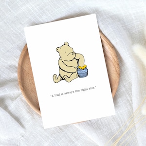 Puede incluir: Una ilustraci&oacute;n de dibujos animados de un oso blanco sosteniendo un tarro de miel azul y amarillo. El texto "A hug is always the right size." est&aacute; debajo de la ilustraci&oacute;n.