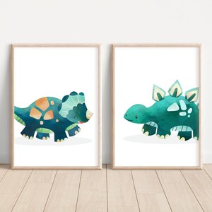 May include: Two framed watercolor illustrations of dinosaurs. The first illustration features a blue and green triceratops. The second illustration features a blue and green stegosaurus.