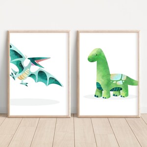 May include: Two framed prints featuring watercolor illustrations of dinosaurs. The print on the left shows a blue and green pterodactyl with its mouth open. The print on the right shows a green brachiosaurus with a light blue and green pattern on its back.