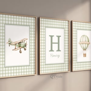 Op de afbeelding: Drie ingelijste wandkunstprints. De prints hebben een groen-witte ruitjesrand. De kunst omvat een aquarel vliegtuig, de letter "H" met de naam "Henry" en een heteluchtballon. De frames zijn lichtbruin.