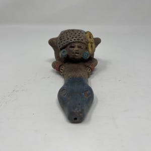 May include: A ceramic pipe shaped like a person riding a snake. The person is brown with blue and yellow accents. The snake is blue and brown.