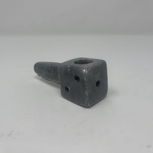 May include: A gray ceramic pipe shaped like a cube with a round hole on the top and a long, thin spout. The pipe has three small holes on the side.