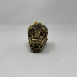 May include: A small, detailed, carved, beige and brown figurine of a dragon's head.