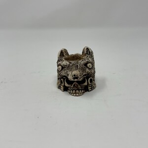 May include: A small, white ceramic planter shaped like a wolf's head with detailed carvings. The planter has a skull-like design with two eyes and a mouth.