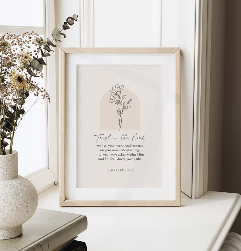 May include: A framed print with the text "Trust in the Lord" and a floral illustration. The print has a light wood frame and is displayed on a white surface. The text includes a Bible verse from Proverbs 3:5-6.