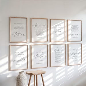 May include: A collection of eight framed art prints with inspirational quotes in black script on white backgrounds. The frames are light wood. The prints are arranged on a white wall, with a decorative vase and small wooden stool in front.