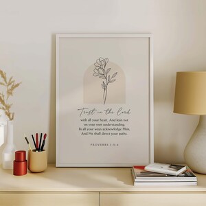 May include: A framed print with the words "Trust in the Lord" and a floral illustration. The print includes a Bible verse from Proverbs 3:5-6. The artwork is in a white frame and has a neutral color palette.