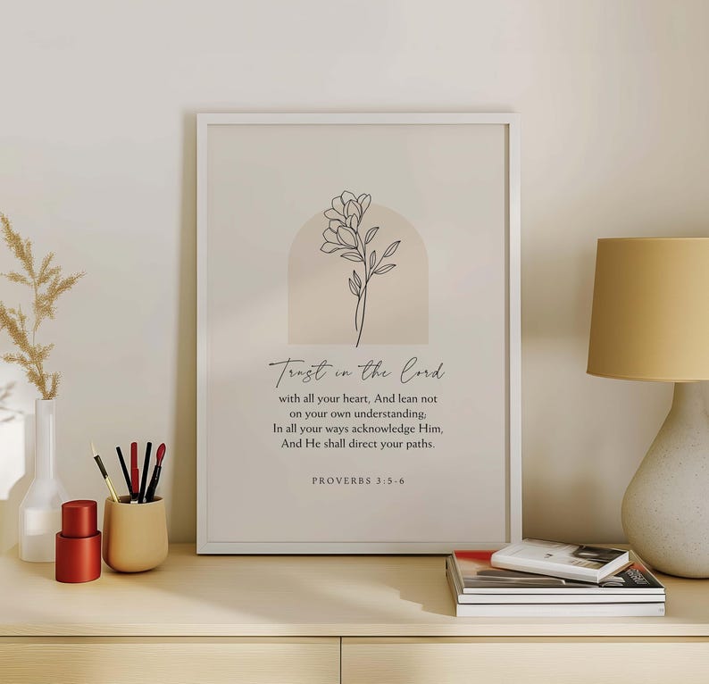 May include: A framed print with the words "Trust in the Lord" and a floral illustration. The print includes a Bible verse from Proverbs 3:5-6. The artwork is in a white frame and has a neutral color palette.