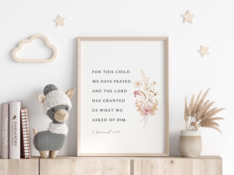 May include: A framed print with the text "FOR THIS CHILD WE HAVE PRAYED, AND THE LORD HAS GRANTED US WHAT WE ASKED OF HIM." Floral illustrations and a stuffed llama toy are on a wooden shelf.