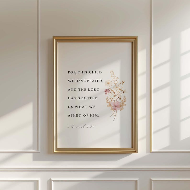 May include: A framed print with a gold-colored frame. The print features text and a floral illustration in soft pinks and creams. The text reads "FOR THIS CHILD WE HAVE PRAYED, AND THE LORD HAS GRANTED US WHAT WE ASKED OF HIM. 1 Samuel 1:27."