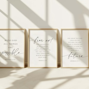 May include: Three framed art prints with inspirational quotes in black script on a white background. The frames are a light brown colour. The quotes include "With God all things are possible," "Fear not," and "Future."