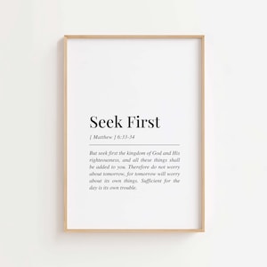 Puede incluir: Un cuadro enmarcado con el texto "Seek First" en un diseño minimalista. La impresión incluye un versículo bíblico de Mateo 6:33-34, con una fuente simple y elegante. El marco es de color madera clara y el fondo es blanco.